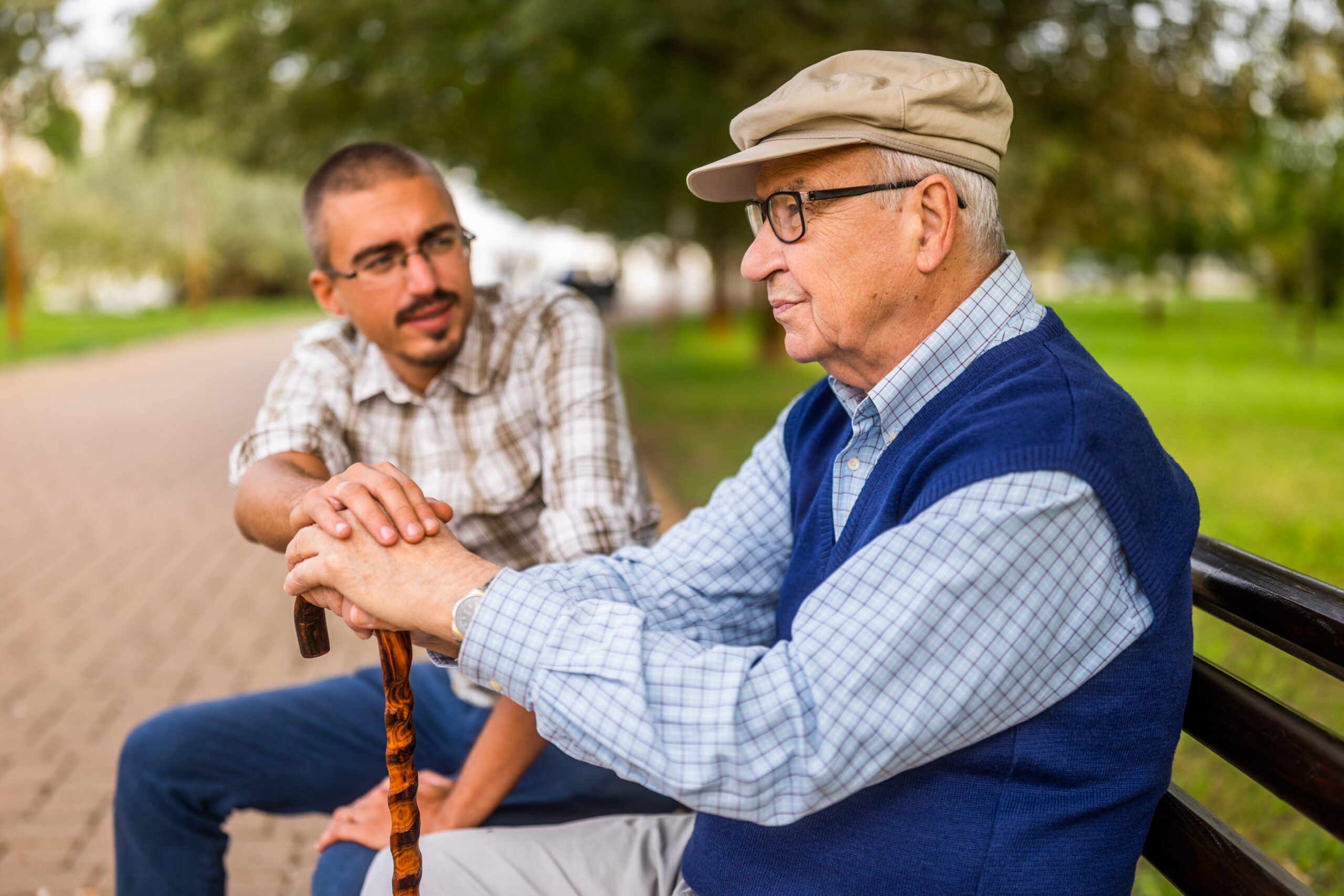 Portrait of grandfather and grandson in park. Old man is worried and concerned but his grandson is consoling him.