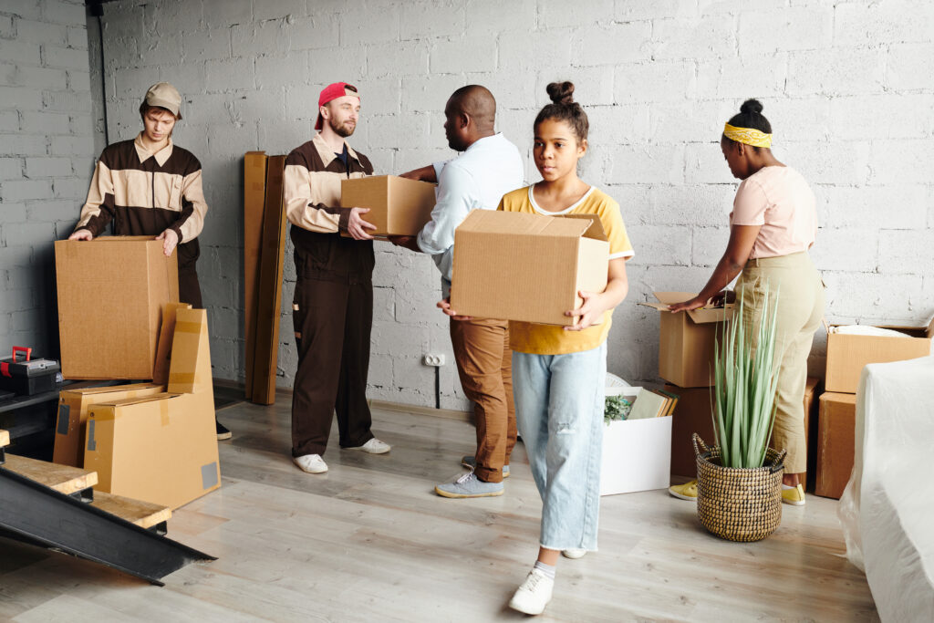Pretty teenage girl of African ethnicity carrying packed cardboard box while helping her elderly father and mother with moving to a retirement residence.